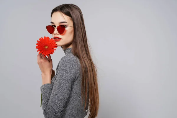 Jolie femme avec fleur rouge près du visage maquillage lumineux gros plan — Photo