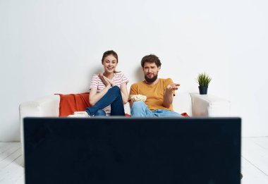 Kadın ve erkek kanepede oturup patlamış mısır eğlencesi izliyorlar.