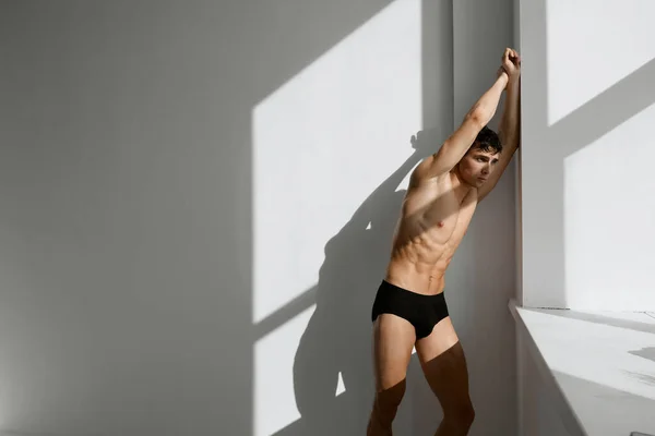 Homem desportivo em shorts pretos com um corpo bombeado posando fundo de luz — Fotografia de Stock