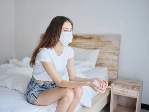 Giovane donna in maschera medica seduta sul letto in camera isolata quarantena pandemia salute — Foto Stock