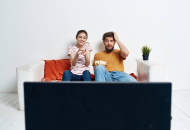 Kadın ve erkek kanepede oturup patlamış mısır eğlencesi izliyorlar.