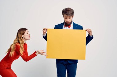 Kırmızı elbiseli bir kadının yanında takım elbiseli bir adam. Sarı model poster reklamı.