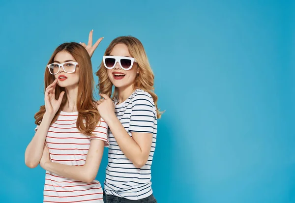티셔츠입은 귀여운 두 여자 친구가 재미있는 파란 안경 배경을 껴안고 있습니다. — 스톡 사진