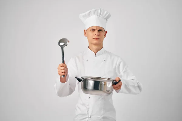 En man i kockuniform med en stekpanna och en slev i händerna som lagar mat — Stockfoto