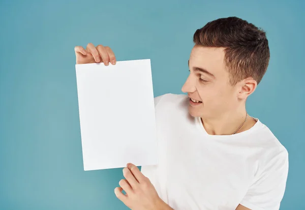 Bel homme en t-shirt blanc avec feuille de papier blanc dans ses mains paperspace fond bleu — Photo