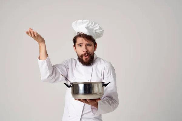Um homem de uniforme de chefs com uma panela em suas mãos preparando comida luz de fundo — Fotografia de Stock