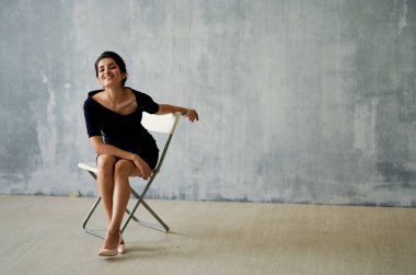 Siyah elbiseli bir kadın poz veren bir sandalyede oturuyor. Moda stüdyosu lüksü.