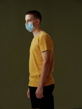 Siyah arka planda sarı tişörtlü bir adamın tıbbi maskesi. Güvenlik aşısı.