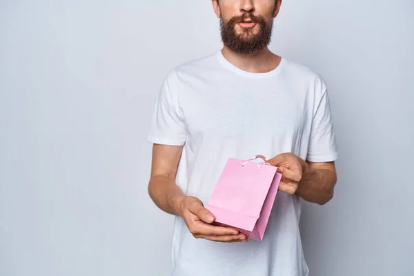 Um homem em uma camiseta branca segurando um presente de presente de pacote rosa presente — Fotografia de Stock