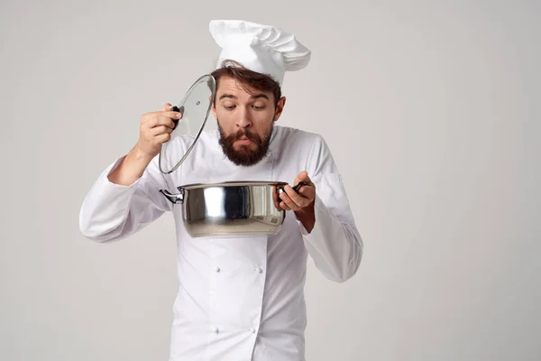 Een man in een koks uniform met een pan in zijn handen het bereiden van voedsel lichte achtergrond — Stockfoto