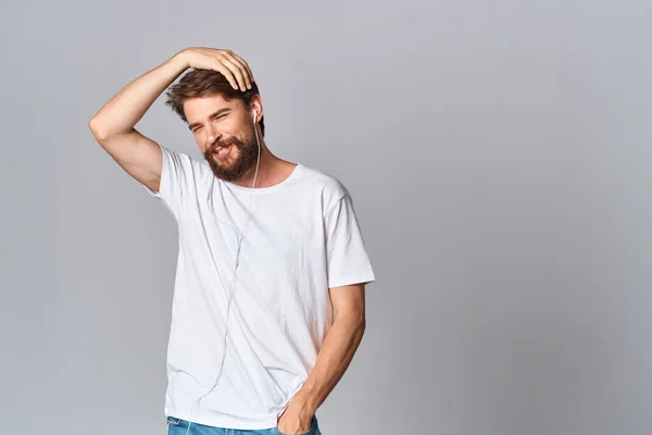 Бородатый мужчина в белой футболке с наушниками, слушающий музыку — стоковое фото