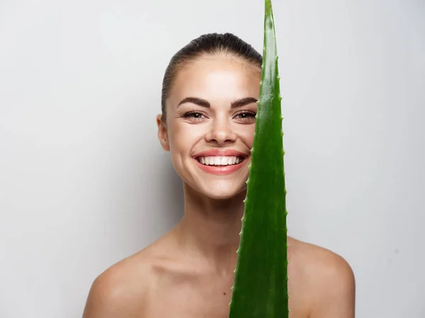 Mulher atraente olha para uma folha verde diante de seus olhos e sorri em um fundo leve — Fotografia de Stock