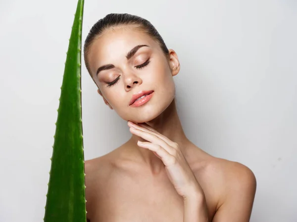 Bela mulher com olhos fechados e folha de aloés verde no fundo claro — Fotografia de Stock