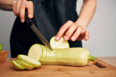 Siyah önlüklü bir kadın sebze doğruyor. Mutfakta yemek pişiriyor.