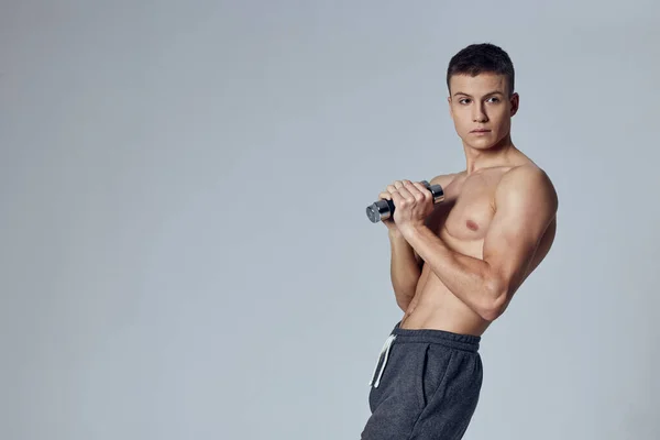 Sport férfi rövidnadrágban súlyzó kezekben edzés tornaterem szürke háttér — Stock Fotó