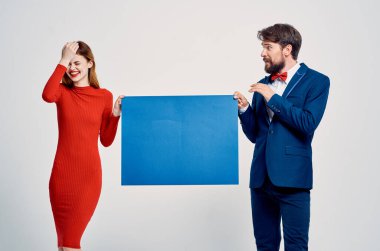 Kırmızı elbiseli kadının yanındaki takım elbiseli adam mavi model tanıtım afişi.