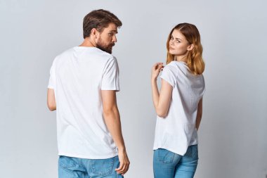 Beyaz tişörtlü erkek ve kadın, arka planlarında hafif bir modelle ayakta duruyorlar.
