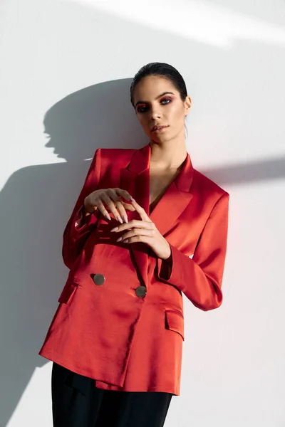 Uma mulher em uma jaqueta vermelha fica perto de uma parede branca e uma sombra caindo — Fotografia de Stock