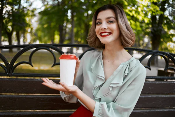 Женщина сидит на скамейке в парке с горячим напитком на открытом воздухе — стоковое фото