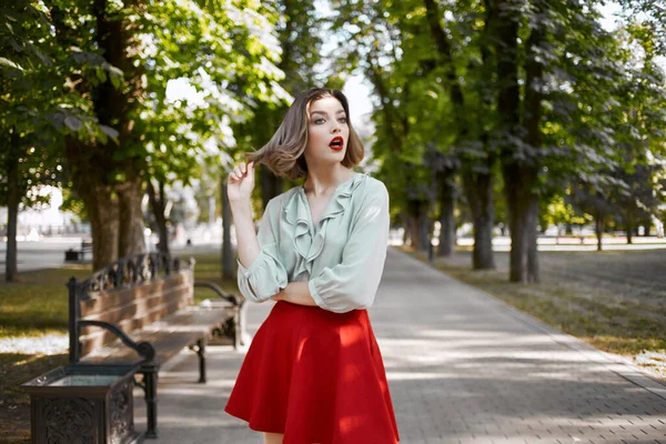 Mooie blonde in rode rok buiten in het park groene bomen — Stockfoto