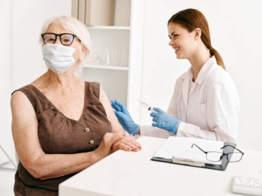 Hemşire yaşlı kadına iğne yapıyor. Hasta aşılama güvenliği için.