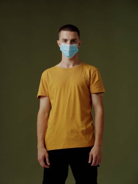 Tıbbi maskeli bir adam covid-19 koyu arka plan sarı tişörtlü.