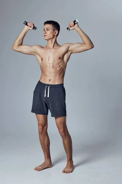 Спортсмен с накачанным телом в шортах тренируется с гантелями в руках мышц — стоковое фото