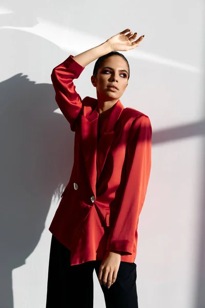 Modieuze vrouw in een rood jasje en zwarte broek houdt haar hand boven haar hoofd — Stockfoto