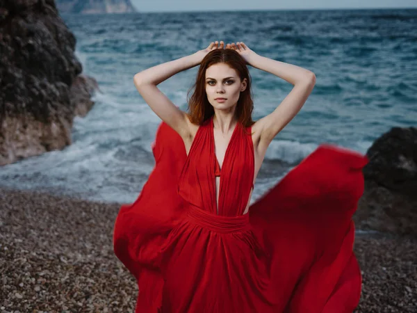 Γυναίκα σε κόκκινο φόρεμα κοντά στον ωκεανό αναρρίχηση μόδας — Φωτογραφία Αρχείου