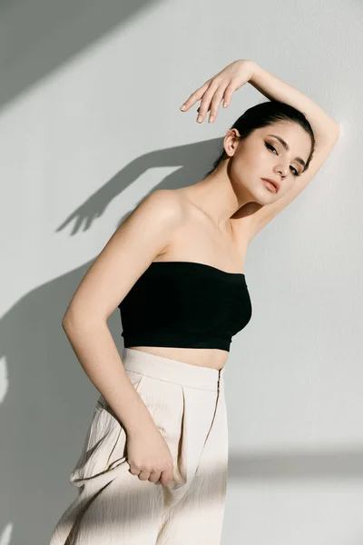 Stylish woman model leaning her hand on white wall indoors makeup pants top — Stock Photo, Image