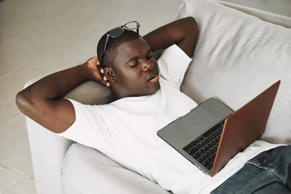 Мужчина африканского появления дома перед ноутбуком, лежащим на диване — стоковое фото
