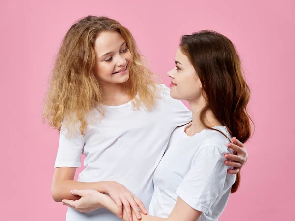 Mamá e hija en camisetas blancas abraza familia alegría fondo rosa — Foto de Stock
