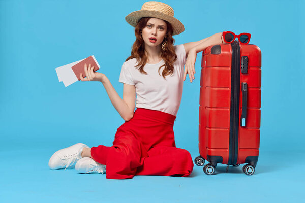 cheerful woman in hat sitting on the floor with red suitcase 