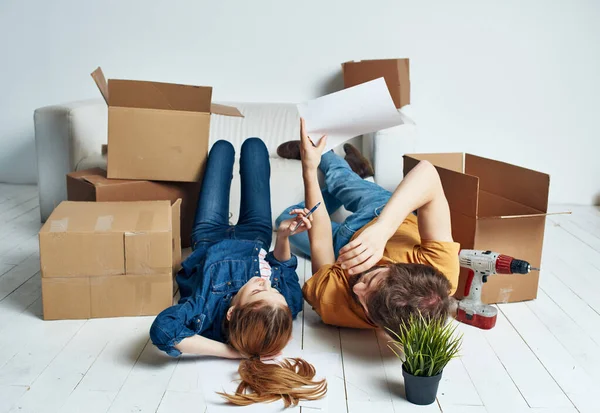 Ένας άντρας και μια γυναίκα ξαπλώνουν στο πάτωμα δίπλα σε κουτιά ανακαινίζοντας ένα δωμάτιο κινούμενοι — Φωτογραφία Αρχείου
