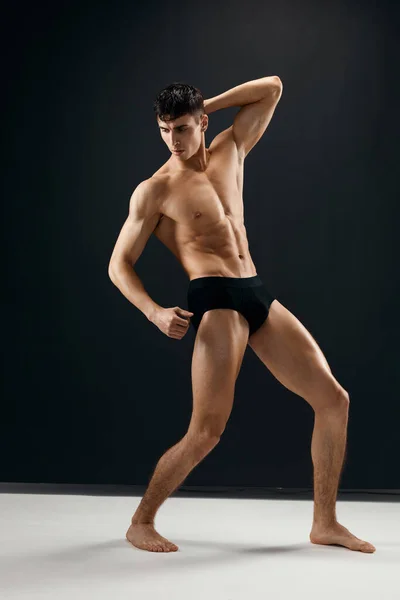 Man with a pumped up muscular body in black panties posing against a dark background — Zdjęcie stockowe