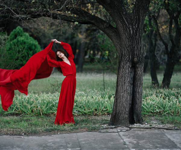 Woman in red dress near tree posing. High quality photo