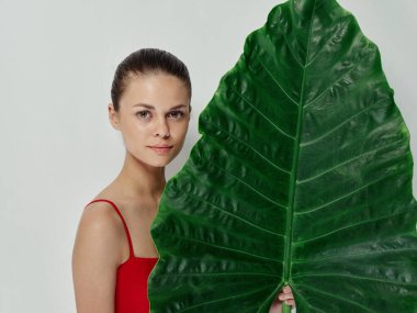 Elinde palmiye yaprağı kırmızı mayo tutan güzel bir kadın. Egzotik bir stüdyo.