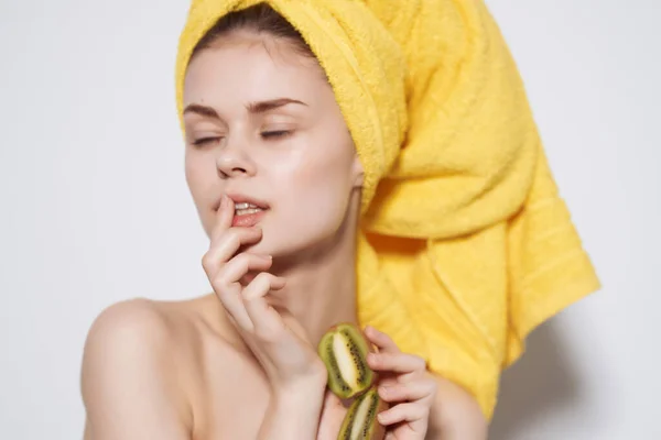 Vrouw met blote schouders met een gele handdoek op haar hoofd kiwi in haar handen schone huid — Stockfoto