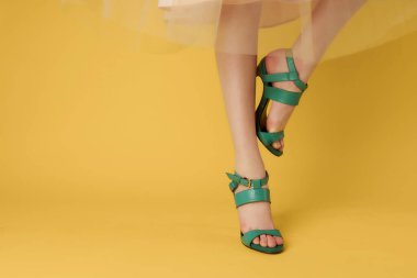 Kadın bacaklarında yeşil ayakkabılar yakın plan sarı arka plan pozu veriyor.