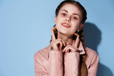 Pembe ceketli, saçları örgülü neşeli bir kadın. Gülümsüyor, makyaj yapıyor.