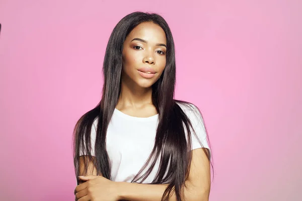 Bonita mujer africana aspecto largo peinado blanco camiseta rosa fondo — Foto de Stock