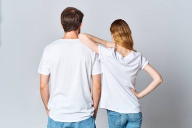 Beyaz tişörtlü erkek ve kadın, arka planlarında hafif bir modelle ayakta duruyorlar.