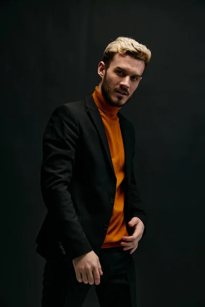 Stijlvol man model in een oranje trui en jasje houdt zijn hand op zijn riem op een donkere achtergrond — Stockfoto