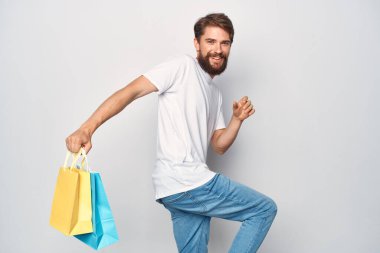 Elinde paketleri olan beyaz tişörtlü bir adam eğlence dünyasında yürüyor.