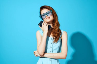 Mavi arka planda telefon ve gözlüklü bir kadının portresi.