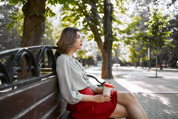 Mujer en falda roja en el parque en el banco al aire libre — Foto de Stock