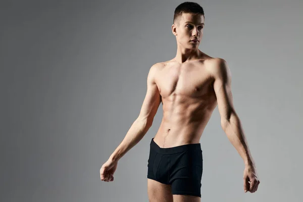 Atleta sexy em shorts pretos em um fundo cinza fisiculturista bíceps modelo — Fotografia de Stock