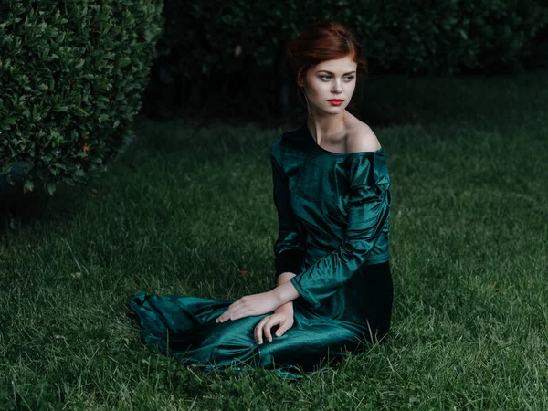 Γυναίκα σε πράσινο φόρεμα βρίσκεται στο γρασίδι που θέτουν glamor μεταμφίεση κήπο — Φωτογραφία Αρχείου