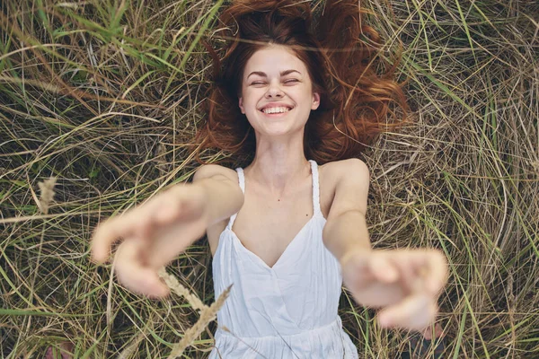 Kollarını kaldırıp çimlere uzanmış beyaz elbiseli neşeli bir kadın. — Stok fotoğraf