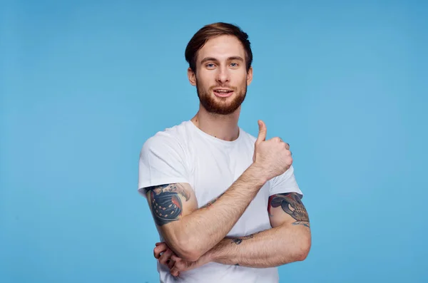 Uomo allegro con tatuaggi sulle braccia in una t-shirt bianca su uno sfondo blu — Foto Stock